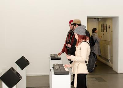 Three people playing keyboards in a gallery.