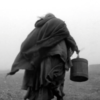 Blacj and white image of the back of a person holding a bucket.