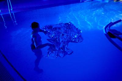 Person in a dark swimming pool with a shiny material.