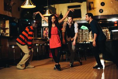 Four people dancing, with a woman wearing a red dress in the middle.
