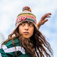 Female dancer in green and white top and colourful hat looking to the left.